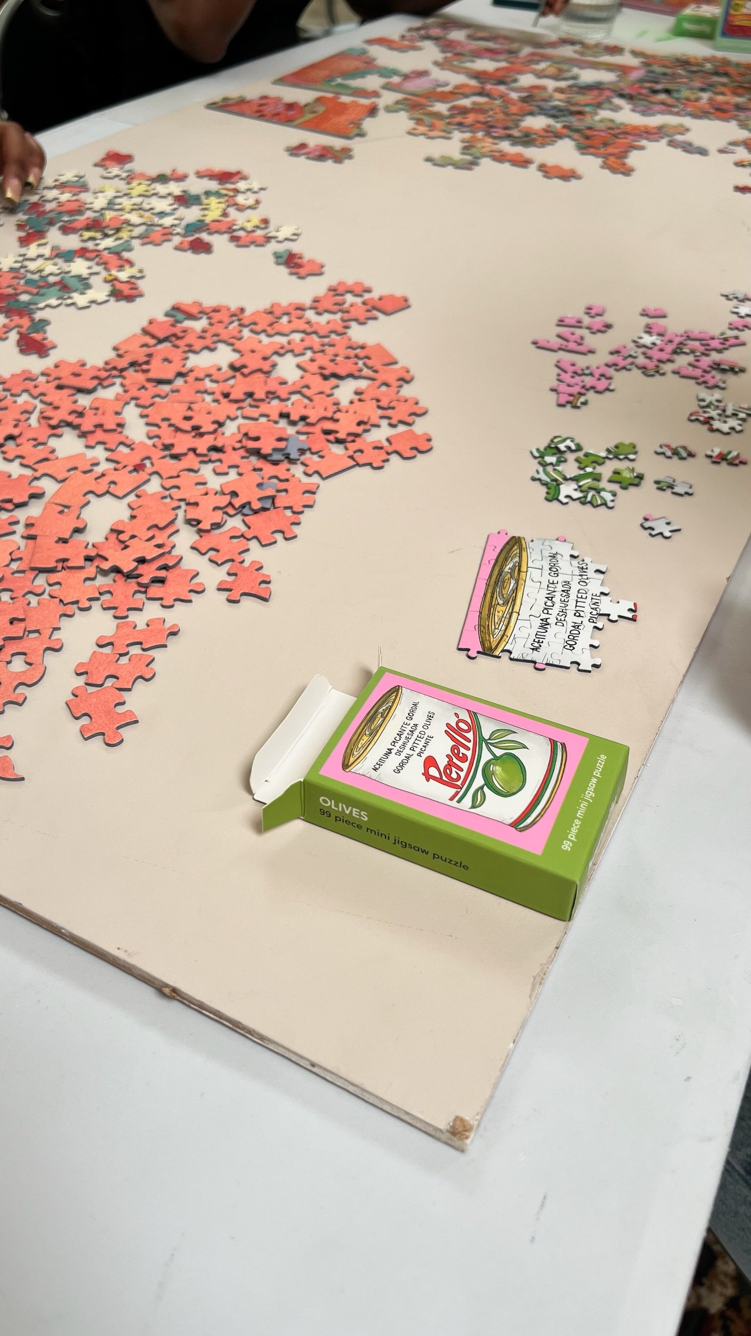 A colourful puzzle mid-assembly with a mini olives puzzle box beside it