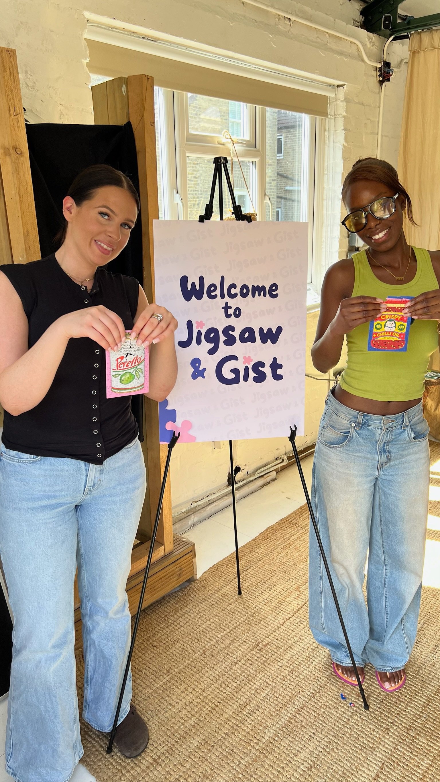 Two people holding up mini puzzle boxes beside the Welcome sign