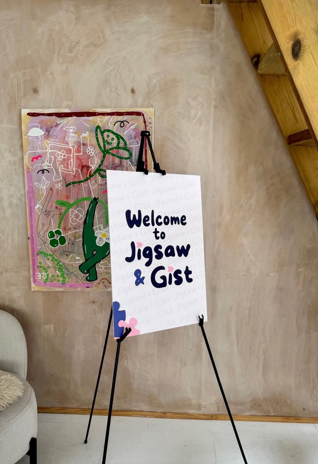 A Welcome to Jigsaw & Gist sign on an easel beside a painting