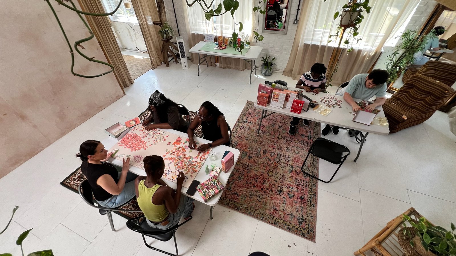 A wide view of the studio with two tables of people puzzling