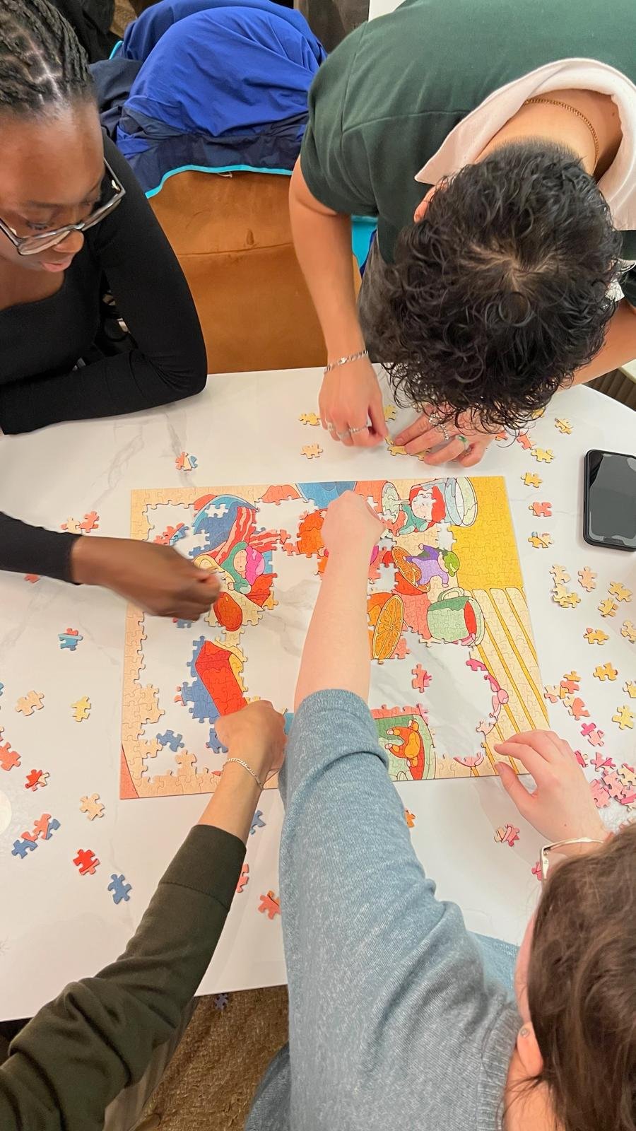 Four hands working together on a colourful puzzle