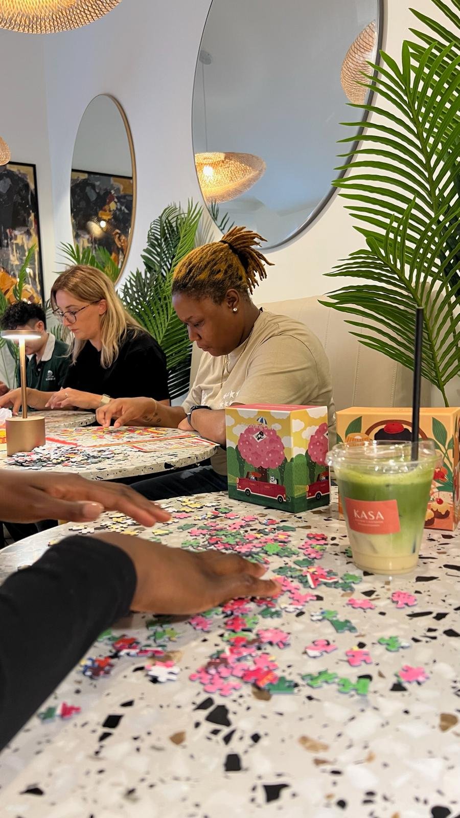 Three women at a table with puzzle boxes and drinks from Kasa Café