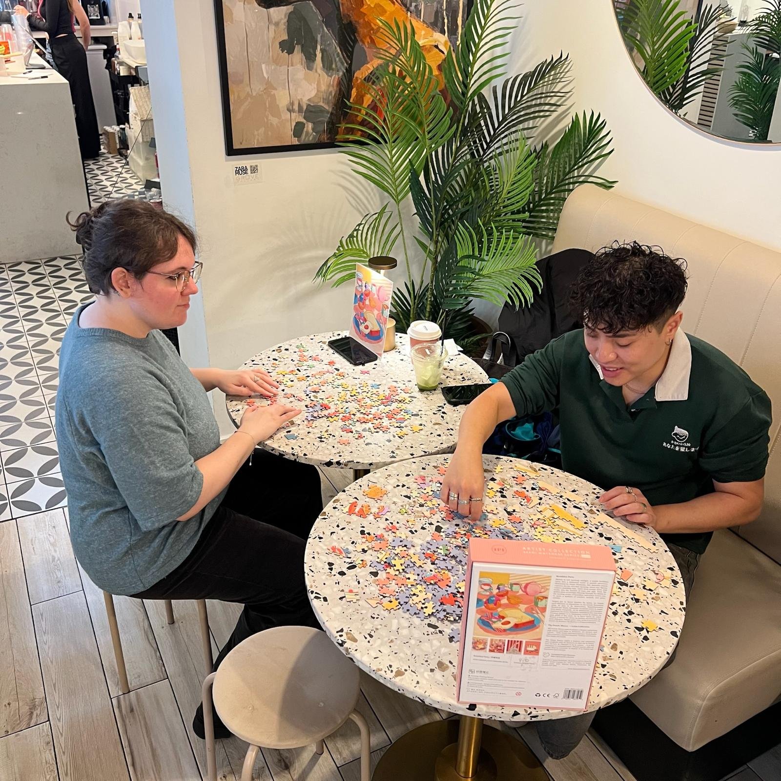 Two women working on puzzles at separate tables in the cafe