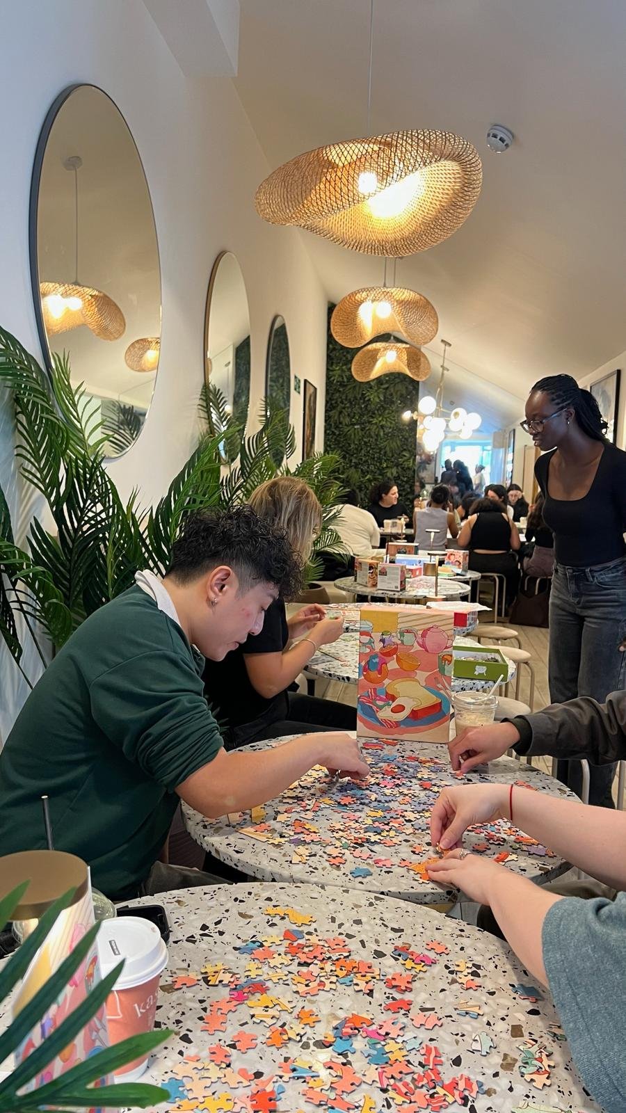 A wide view of the cafe with several tables of people puzzling