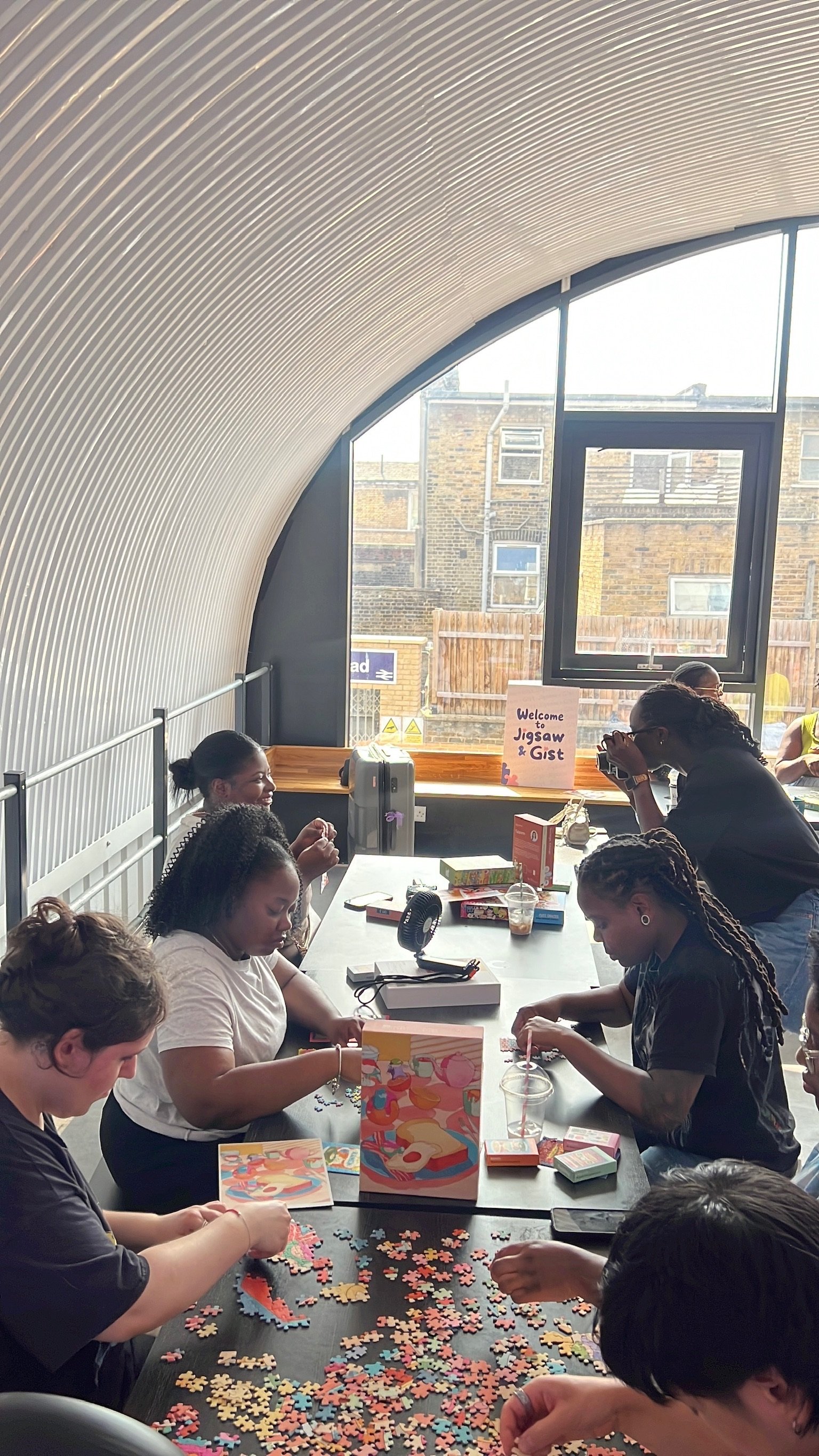 A group gathered by the window next to the Welcome to Jigsaw & Gist sign