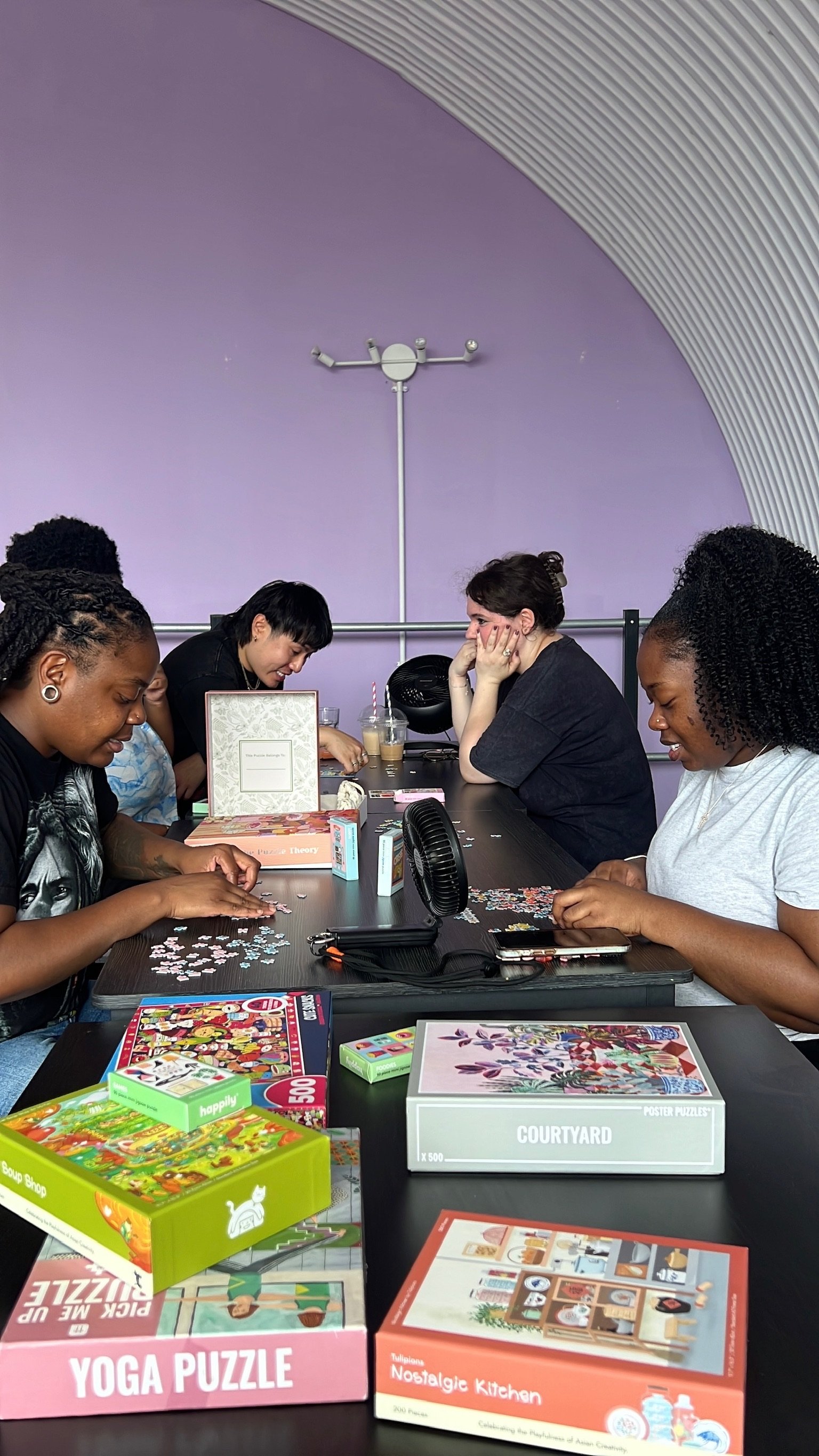 A group working on a puzzle with puzzle boxes stacked on the table